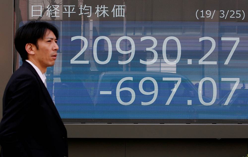 A man walks past an electronic board showing the Nikkei stock index outside a brokerage in Tokyo March 25, 2019. — Reuters pic