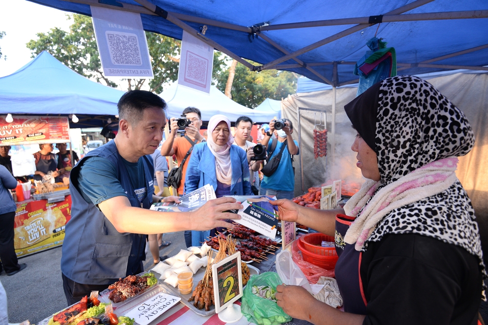 PN Pantai Jerejak candidate Oh Tong Keong giving out his flyer to a vendor during his walkabout at the Pantai Jerejak night market, August 2, 2023. Pictured with him is Datuk Zuraida Kamaruddin. — Picture by KE Ooi
