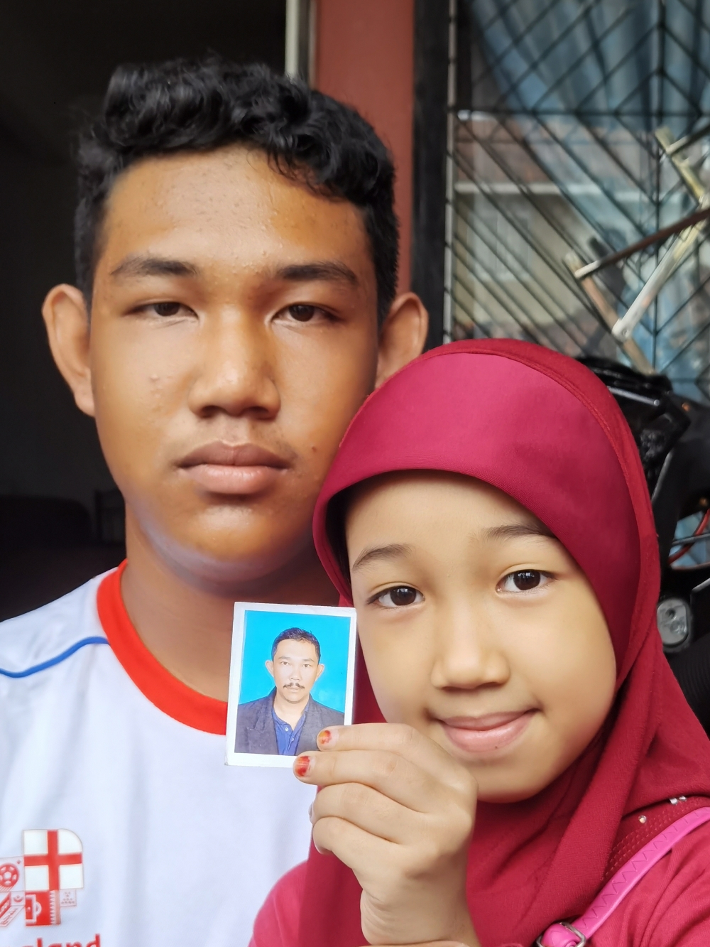 Muhammad Sharul, 16, and his sister Nur Izzara Arissya, 9, show a picture of their father Sharipuddin Shaari who died in a plane crash on the Guthrie Highway near Elmina Town, yesterday evening. — Bernama pic 