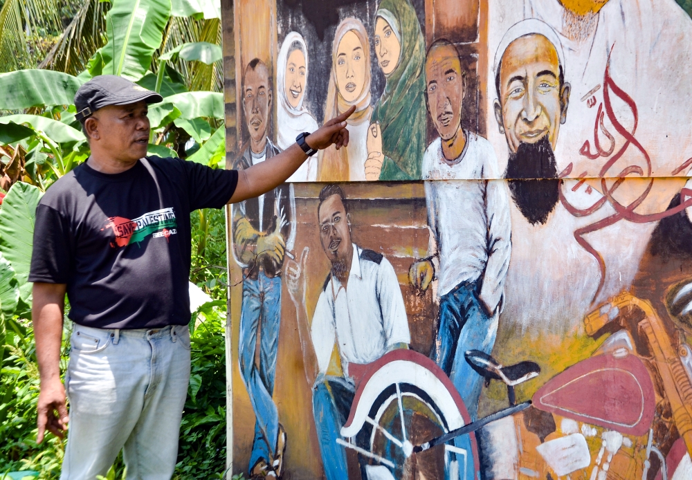 Retired sergeant Ridzwan Abdul Wahab shows some of the portraits he had produced on the wall of his shop in Kampung Bertam Baru September 13, 2023. — Bernama pic