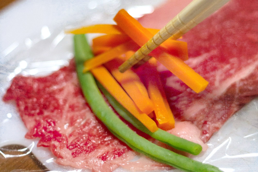 Place the julienned sticks of carrots and green beans on the thinly sliced beef.