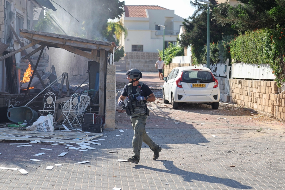 A member of the Israeli forces runs past a fire rages in a house in Ashkelon, following a rocket attack from the Gaza Strip on southern Israel on October 7, 2023. — AFP pic