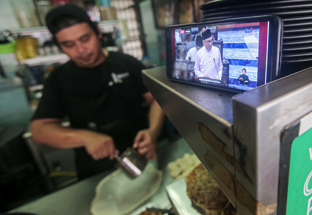 File picture of a hawker watching Prime Minister Datuk Seri Anwar Ibrahim tabling Budget 2024 in Parliament on his smartphone. The Human Resources Ministry said skills improvement and re-skilling initiatives tabled under Budget 2024 will be implemented through the allocation of RM1.6 billion for 1.7 million training placements. — Picture by Farhan Najib