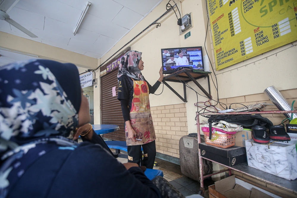 People at a stall at the Ashby Road flats watch the tabling of Budget 2024 on television by Prime Minister Datuk Seri Anwar Ibrahim October 13, 2023. — Picture by Farhan Najib