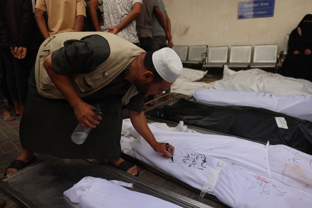 A Palestinian man writes the names of victims from the al-Hamayda family on the shrouds wrapping their bodies at the Al-Najjar Hospital following an Israeli air strike on Rafah in southern Gaza Strip on October 27, 2023, amid ongoing battles between Israel and the Palestinian Hamas movement. — AFP pic