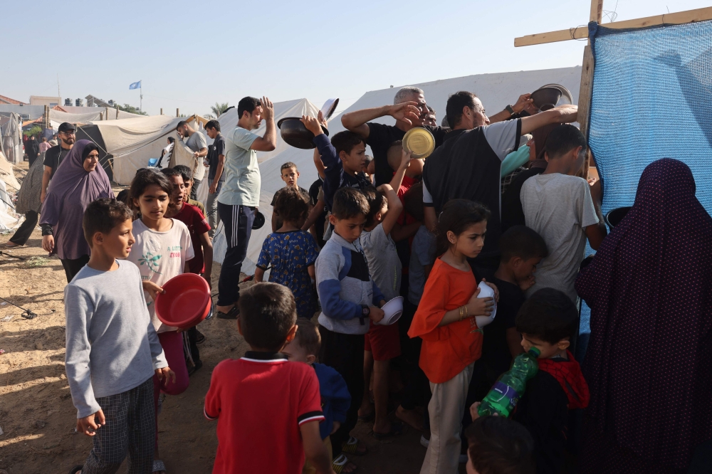 Displaced Palestinians, who fled their houses amid Israeli strikes, wait at a food distribution point as they shelter in tents set up in a United Nations-run centre, following Israel's call for more than one million civilians in northern Gaza to move south, in Khan Yunis, in the southern Gaza Strip on October 26, 2023, amid the ongoing battles between Israel and the Palestinian group Hamas. — AFP pic