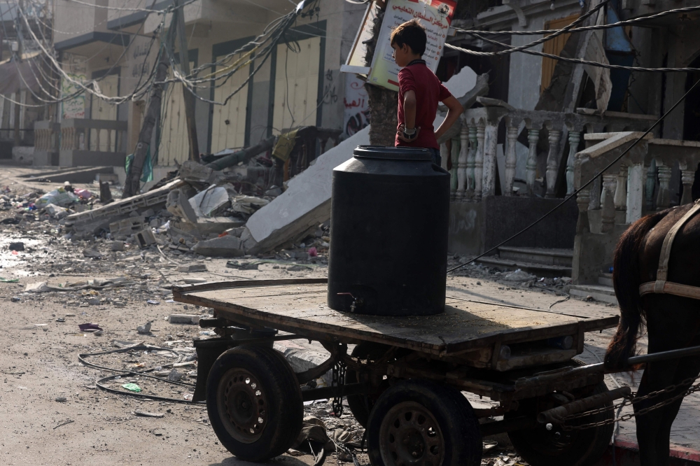 A young boy stands atop a donkey-pulled cart carrying a water container, in the midst of destruction, following Israeli strikes in Gaza City on October 28, 2023. — AFP pic