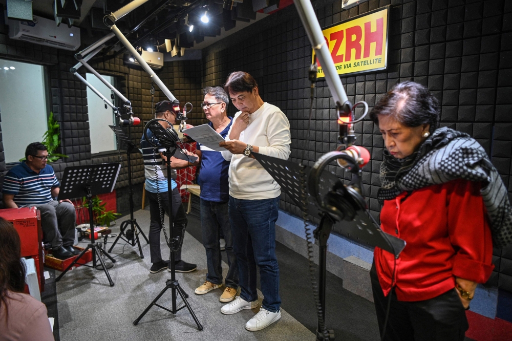 This photo taken on July 17, 2023 shows Phil Cruz (3rd left), his brother Robert (2nd right) and other voice actors recording their part for a radio drama at a studio of a radio station in Manila. — AFP pic