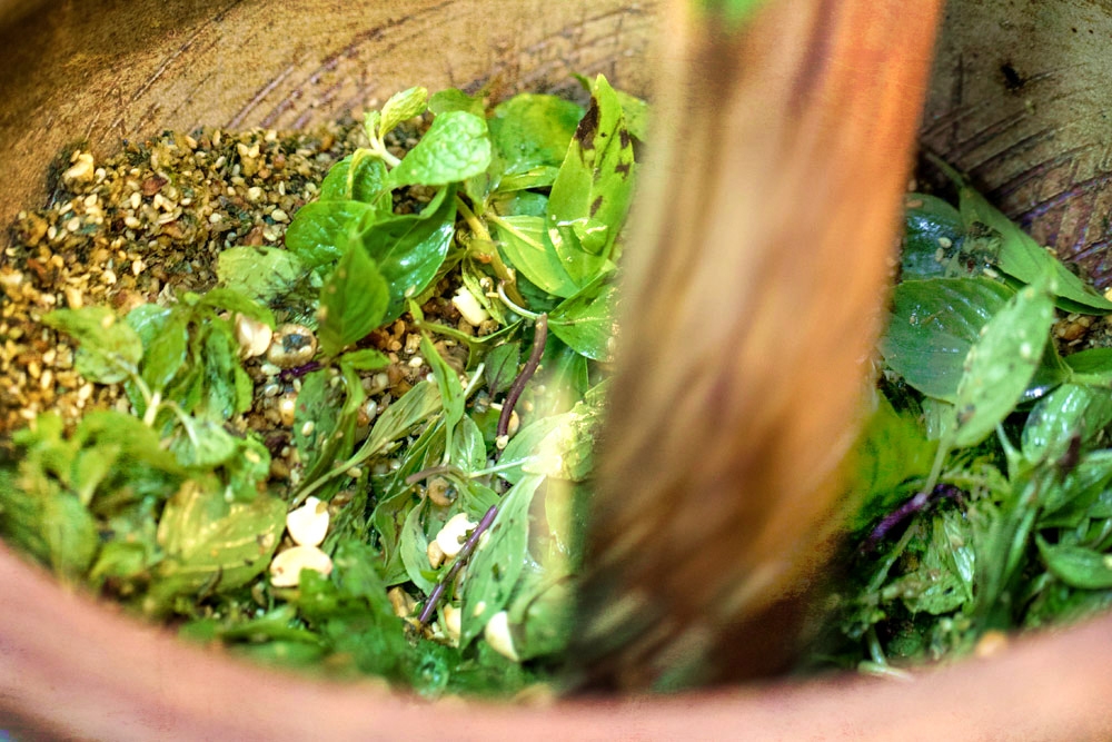 Pounding fresh leaves and seeds to make 'lei cha' paste.