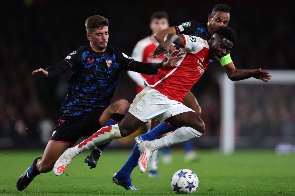 Arsenal midfielder Bukayo Saka is fouled by Sevilla midfielder Fernando Reges and defender Kike Salas during the Uefa Champions League Group B football match between Arsenal and Sevilla at the Emirates Stadium in north London on November 8, 2023. — AFP pic 