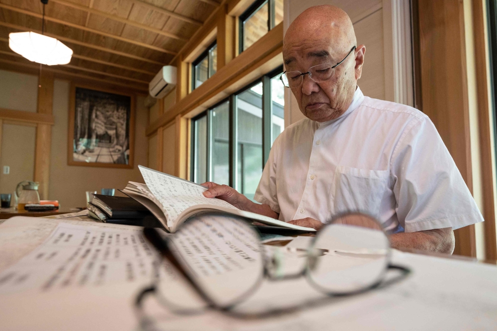 Chief Buddhist priest Eiichi Shinohara looking at a diary of a woman who was swindled out of millions of yen. — AFP pic