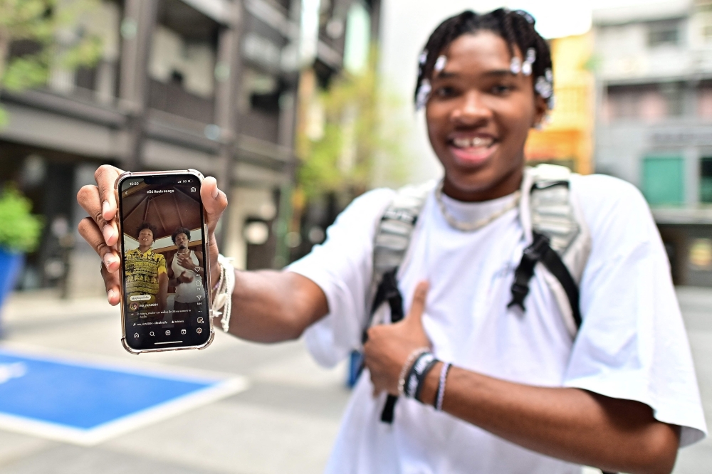 Thai influencer Dalintan 'MoRich' Promphinit posing with his viral post in elephant print pants on his smartphone in Bangkok. — AFP pic