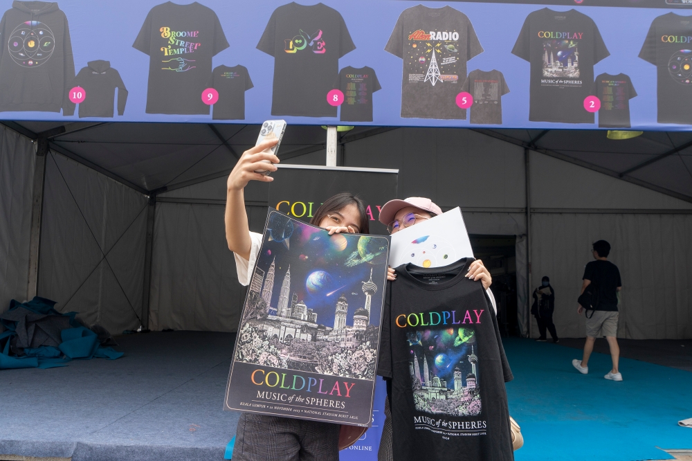 Fans take a picture with Coldplay merchandise at Bukit Jalil National Stadium in Kuala Lumpur on November 22, 2023. — Picture by Shafwan Zaidon