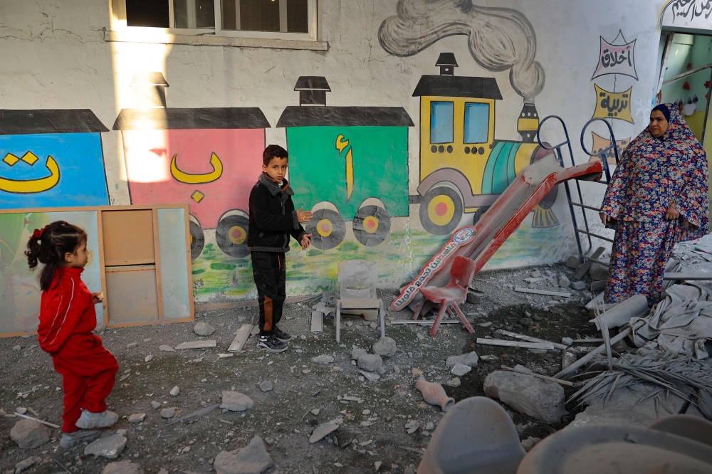 A woman and children stand amid the rubble at a kindergarten hit by Israeli bombing in Rafah in the southern Gaza Strip on December 9, 2023, amid continuing battles between Israel and Hamas. — AFP pic