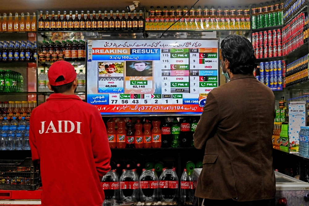 People watch latest election results live on a television at a shop, a day after Pakistan's national elections in Lahore on February 9, 2024. — AFP pic