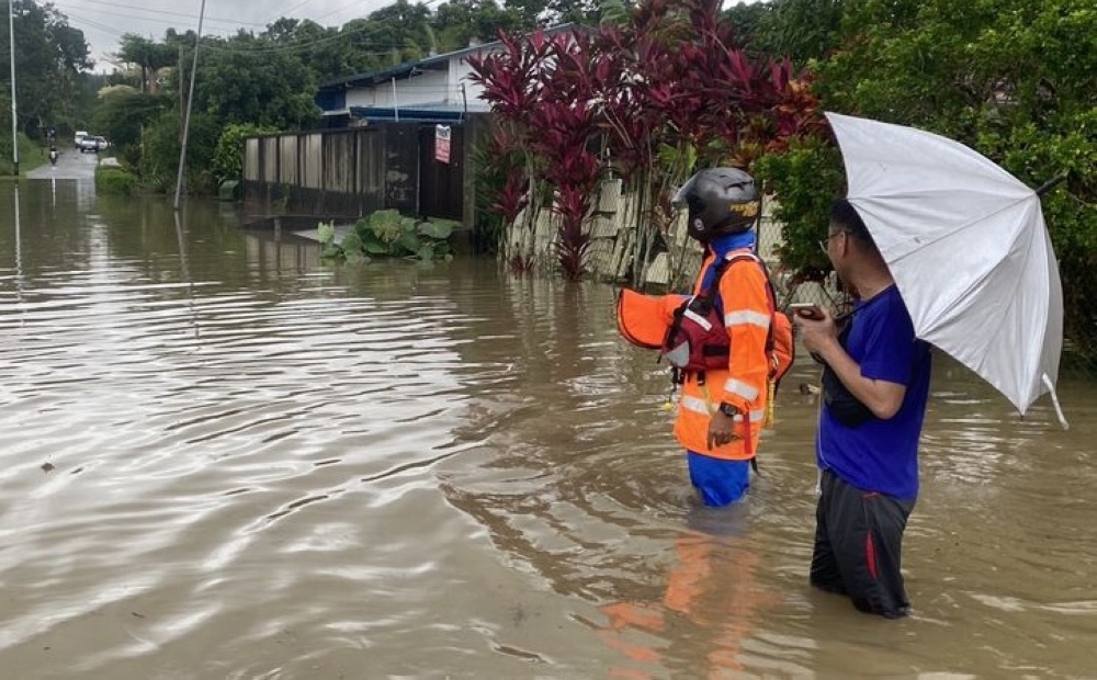 A resident at Jalan Jambori joins a check on the water level along the main road leading to the area. — Picture courtesy of Civil Defence Force