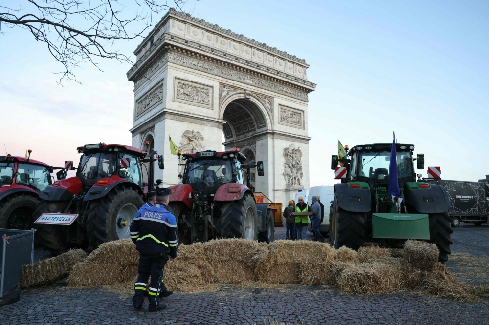 Policemen look at tractors seen parked next to the Arc de Triomphe on the Champs-Elysees Avenue during a protest by the French farmers' union in Paris March 1, 2024. — AFP pic