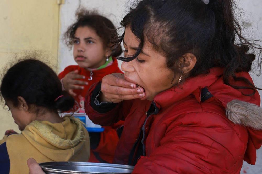 Displaced Palestinian children eat rice out of a bowl near a food distribution point in Rafah in the southern Gaza Strip on March 8, 2024, amid the ongoing conflict between Israel and Hamas militants. — AFP pic