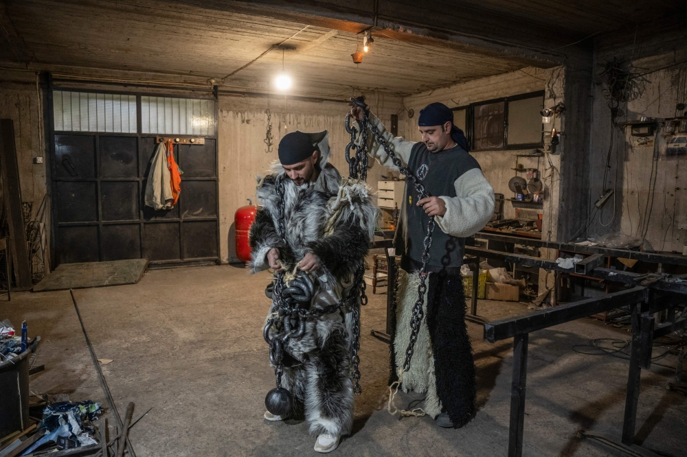 Costas Panagiotas, 42, fireman (right) helps Christos Doukas, 35 (left) to put on his costume at his house prior to the celebration of 