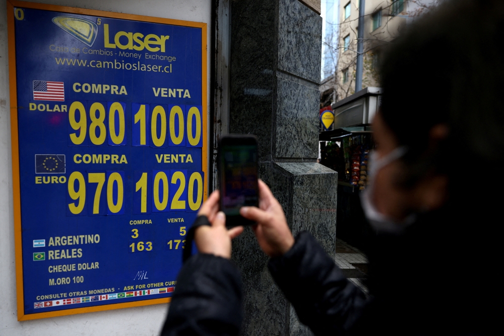 A woman uses a mobile phone to shoot pictures to a sign showing the exchange rate for the U.S. dollar and other currencies in Santiago July 11, 2022. — Reuters pic  