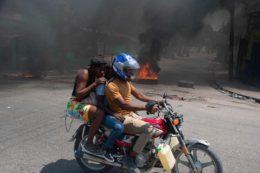 A woman with a child lowers her head as they leave the area on a motorcycle after gunshots were heard in Port-au-Prince, Haiti, on March 20, 2024. — AFP pic