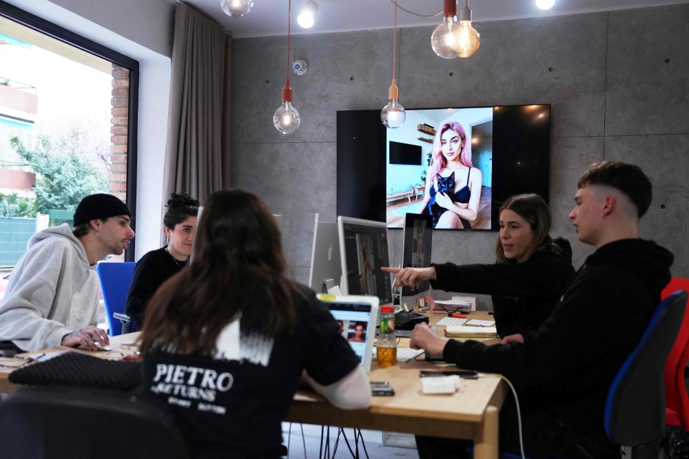 Spanish co-founders and creative directors at The Clueless agency Diana Nunez (second right), Ruben Cruz (left) and other employers work on their computer as an artificial intelligence generated image of Aitana Lopez model is displayed on a screen at the headquarters of The Clueless company in Barcelona, on March 25, 2024. — AFP pic