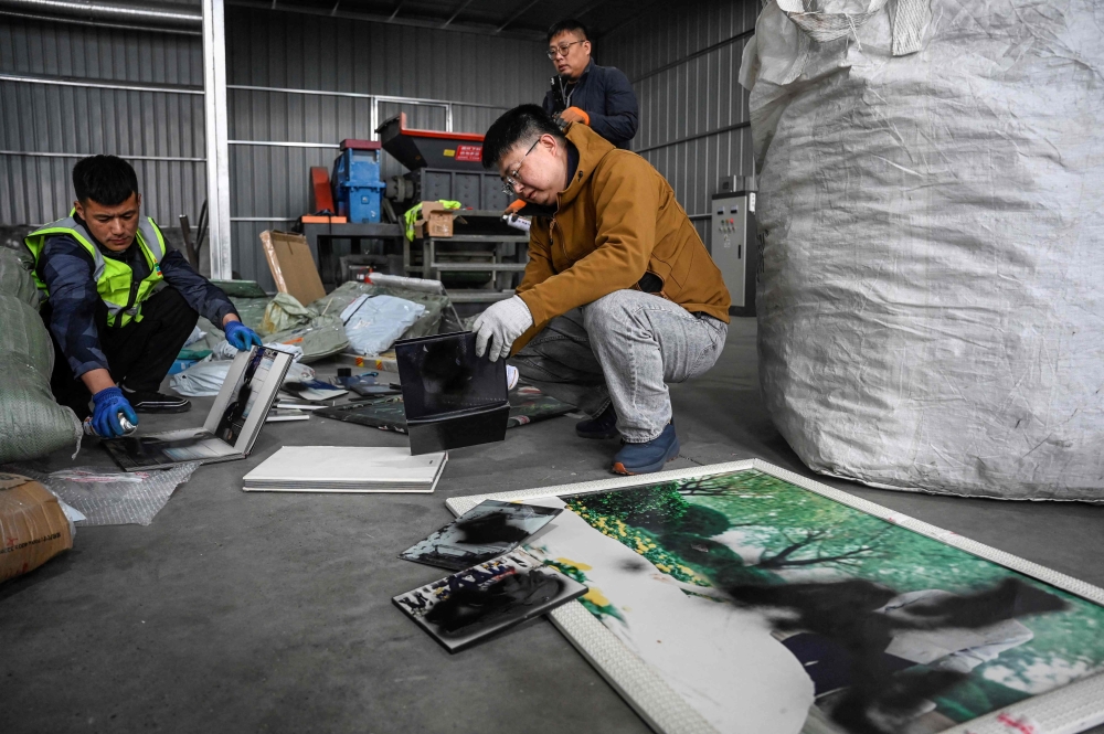 This photo taken on March 27, 2024 shows Liu Wei (right) and workers spraying paint on clients’ unwanted wedding photos at a warehouse in Langfang, in northern China’s Hebei province. — AFP pic
