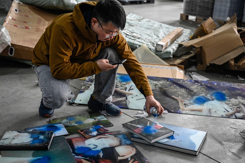This photo taken on March 27, 2024 shows worker Liu Wei spraying paint on clients’ unwanted wedding photos at a warehouse in Langfang. — AFP pic