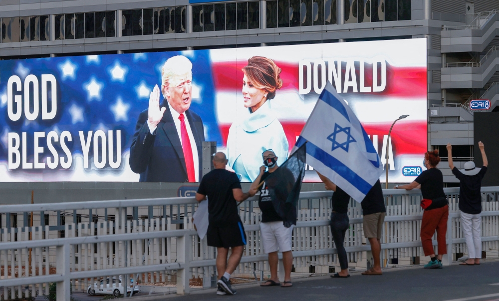 File photo of people lifting a national flag on an overpass facing a large billboard depicting the US President Donald Trump and his wife Melania on a building in the Israeli coastal city of Tel Aviv, on October 3, 2020. — AFP pic