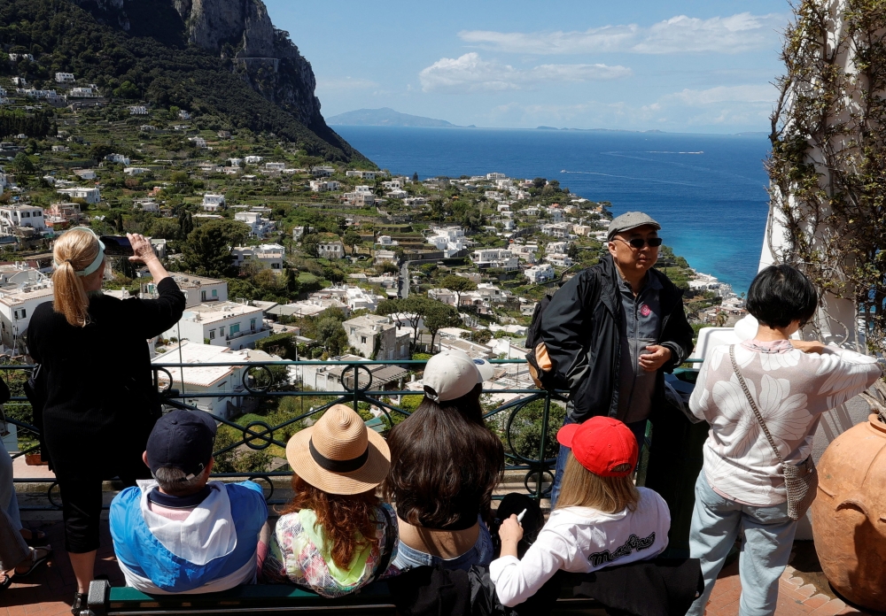 People sit on a bench and take photos on Capri Island, Italy, April 18, 2024. — Reuters pic  