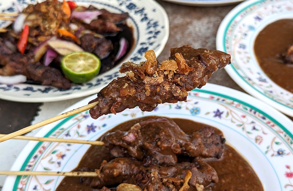 'Sate lembu' comes drenched in the thick peanut-based sauce and topped with fried shallots.