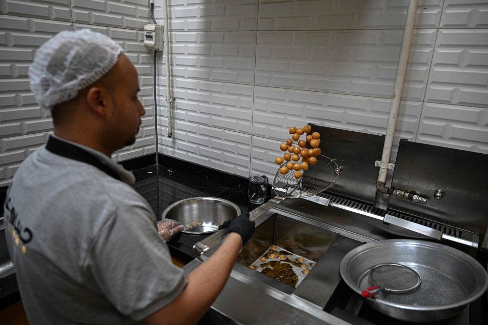 An employee fries sweet pastry with traditional Sudanese taste at a restaurant run by a businessman who relocated to Cairo after fleeing the ongoing war in Sudan May 27, 2024. — AFP pic