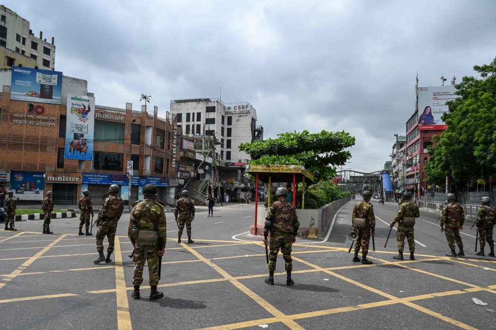 Bangladesh soldiers stand guard along a road following a curfew and the deployment of military forces in Dhaka today after days of clashes. — AFP pic