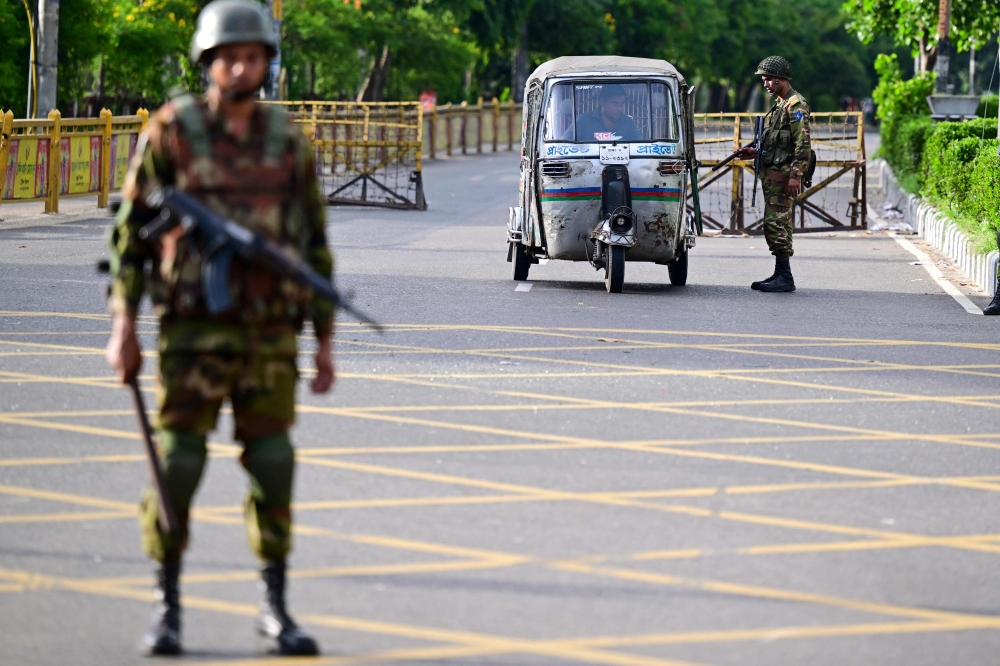 Bangladeshi soldiers stand guard along a street to quell growing civil unrest. — AFP pic