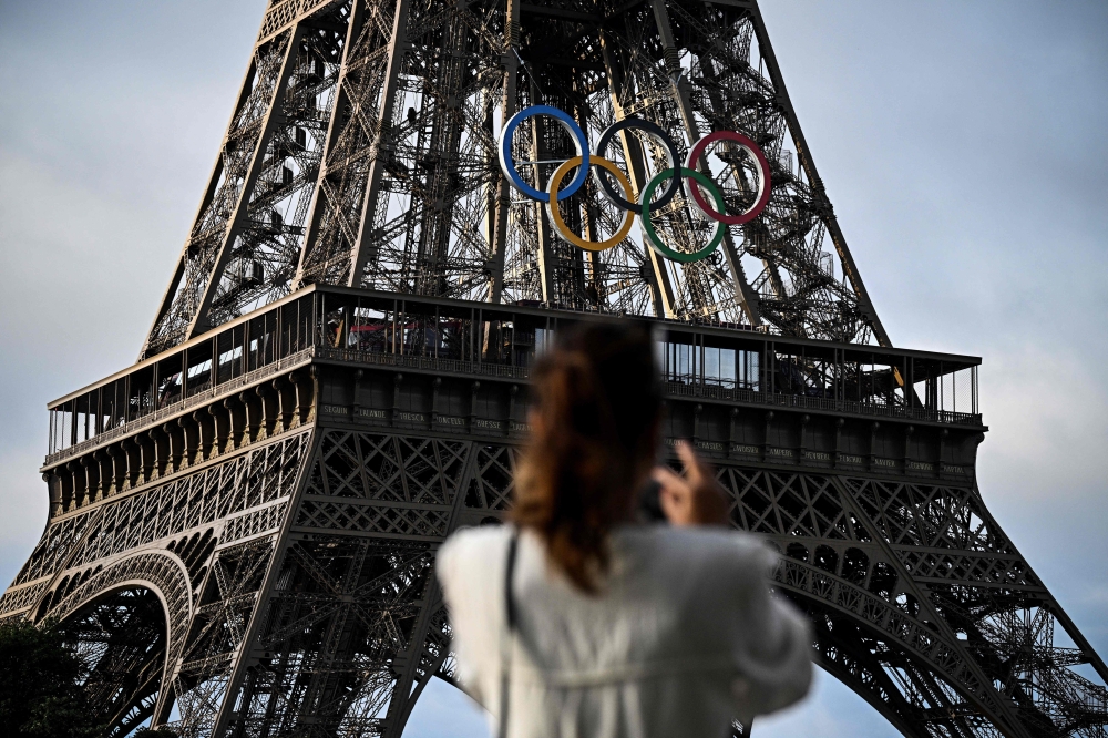 A woman takes a picture of the Eiffel Tower decorated with the Olympic rings for the upcoming Paris 2024 Olympic Games, in Paris June 17, 2024. Olympics news website Insidethegames.biz, which was acquired by a Russian-run fund, says it has been effectively ‘banned’ from the Paris Olympics after its accreditation requests were turned down. — AFP pic