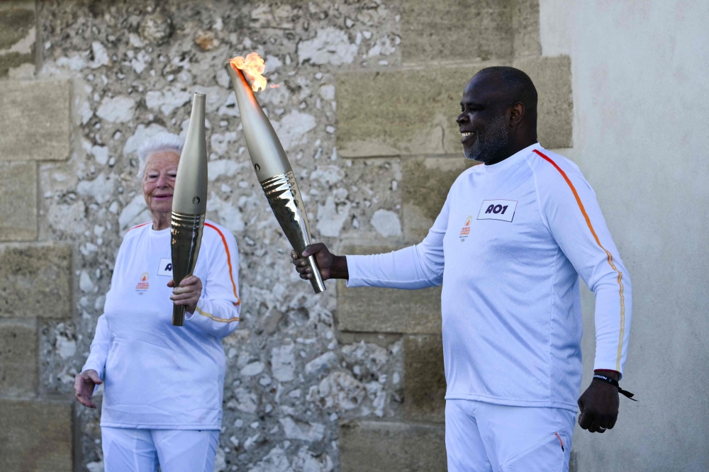 French former football player Basile Boli (right) holds the Olympic Torch and lights up the torch of French founder of Olympique de Marseille supporters club ‘Dodger's Marseille’ Colette Cataldo as part of the Olympic and Paralympic Torch Relays at the Notre Dame de la Garde Basilica, ahead of the Paris 2024 Olympic and Paralympic Games, in Marseille May 9, 2024. — AFP pic