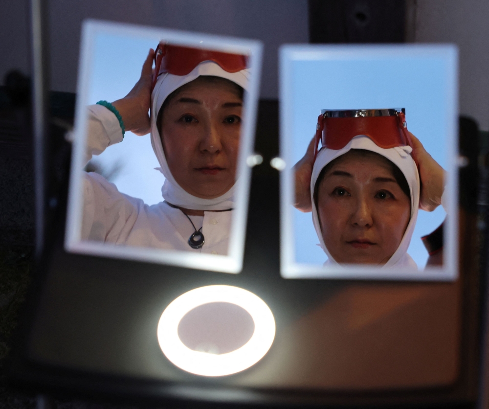 Yoshino Hirano, 53-year-old ‘Ama’, a female free diver, who harvests sea life from the ocean, adjusts her attire as she looks at mirrors while preparing for Shirahama Ama matsuri in Minamiboso, Chiba Prefecture, Japan July 20, 2024. — Reuters pic