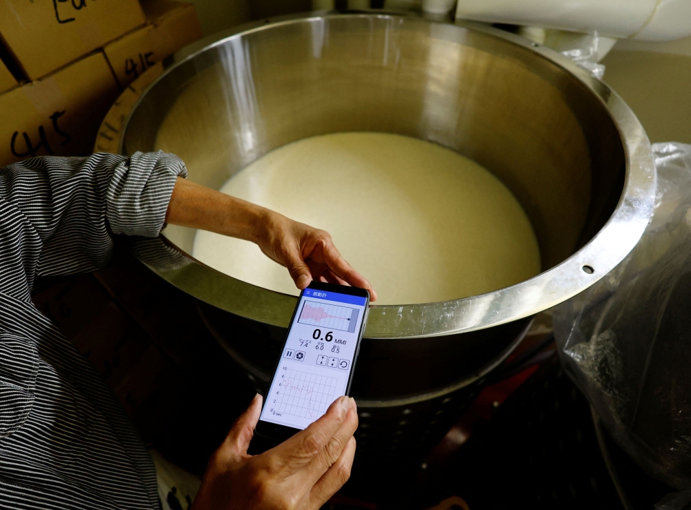 Yoshimi Terasawa, chief brewer at Tokyo Port Brewing, checks vibrations on a tank where a speaker plays music installed beneath it at the brewery in Tokyo July 9, 2024. — Reuters pic