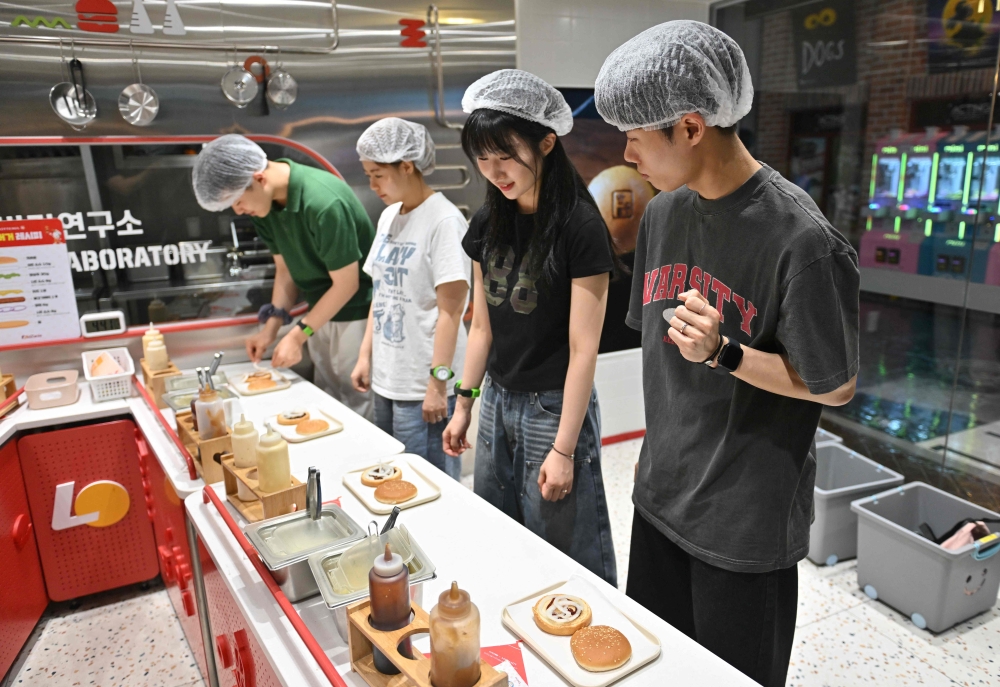 KidZania is part of a Mexican-owned global chain that typically offers young children the chance to play at dozens of different jobs, from firefighter to dentist, in giant indoor centres. Here, visitors role-play as researchers in a mock burger laboratory during an adult-only event in Seoul June 28, 2024. — AFP pic