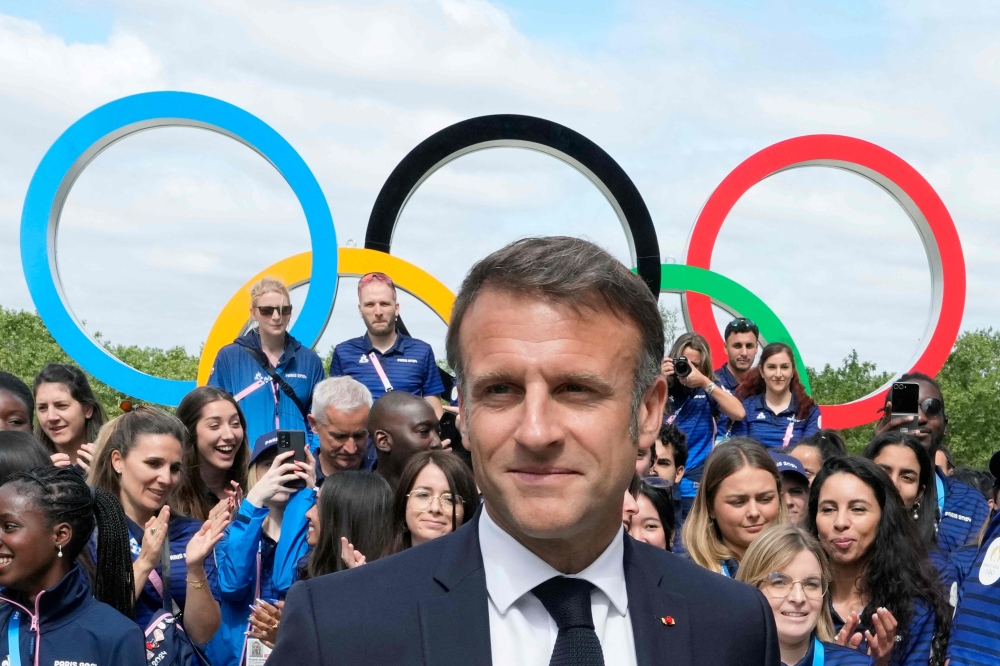 French President Emmanuel Macron looks on with the Olympic rings displayed behind him, leaves after posing with French athletes during a visits at the Olympic Village, in Saint-Denis, northern Paris, on July 22, 2024. — AFP pic