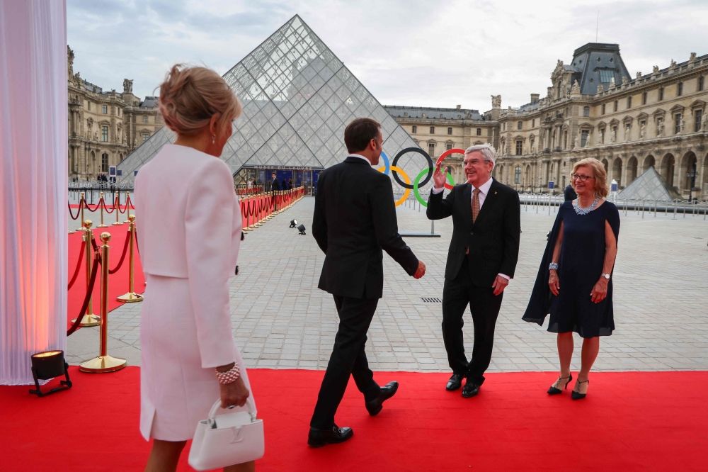 TOPSHOT - President of the International Olympic Committee (IOC) Thomas Bach (2ndR) and his wife Claudia Bach (R) greet French President Emmanuel Macron and his wife Brigitte Macron upon their arrival at the Pyramide du Louvre to attend a gala dinner  on the eve of the opening ceremony of the Paris 2024 Olympic Games. — AFP