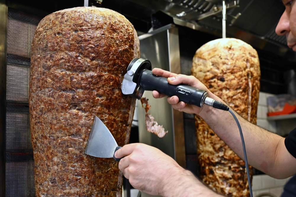 An employee scapes meat from a kebab skewer in a snack bar in the city centre of Dortmund July 26, 2024. — AFP pic
