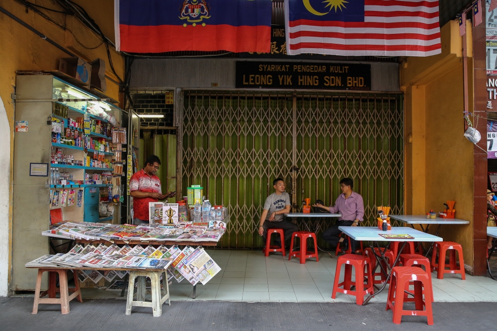 A newspaper vendor checks his mobile phone as two men chat at a food stall in Kuala Lumpur. — Picture by Yusof Mat Isa