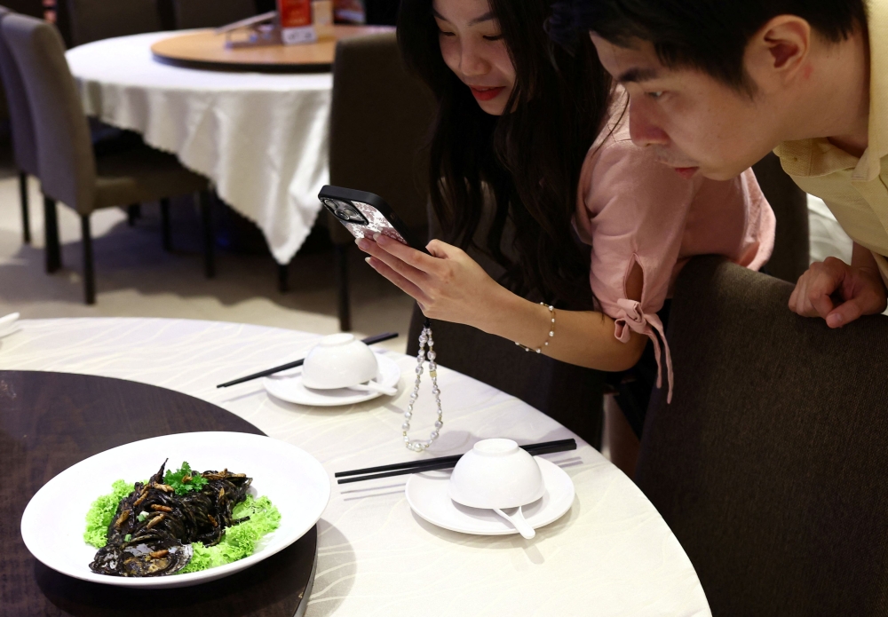 Food tasters take photos of squid ink pasta sprinkled with house crickets at the House of Seafood restaurant in Singapore. — Reuters pic