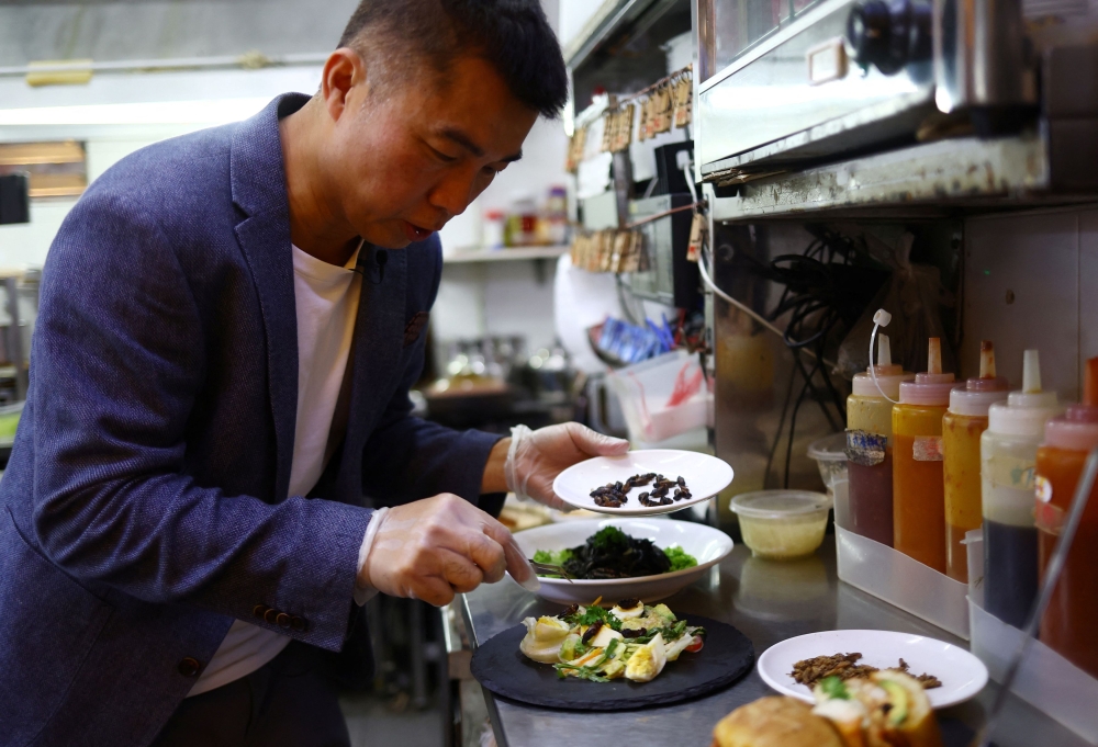 Restaurant owner Francis Ng garnishes a bowl of salad with black field crickets during a showcase of insect-based dishes at the House of Seafood restaurant in Singapore. — Reuters pic