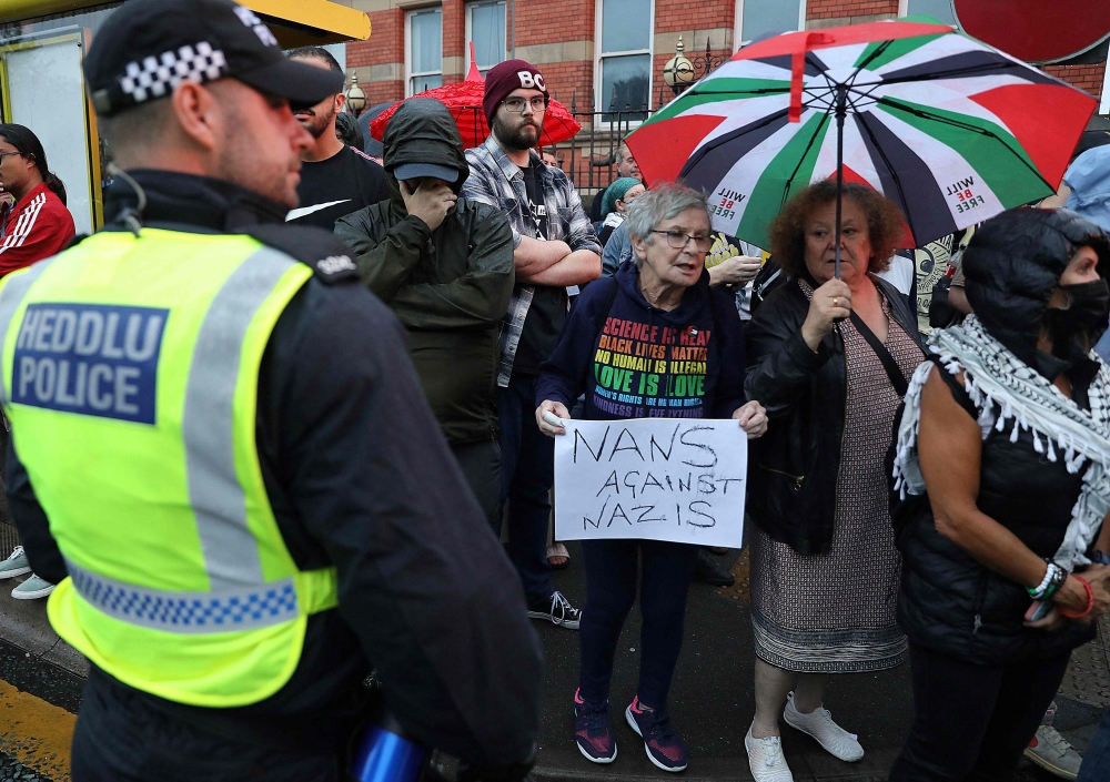 A police officer stands guard in front of protesters defending the Abdullah Quilliam Mosque in Liverpool on August 2, 2024 against the ‘Enough is Enough’ demonstration (not seen) called in reaction to the fatal stabbings in Southport on July 29. — AFP pic