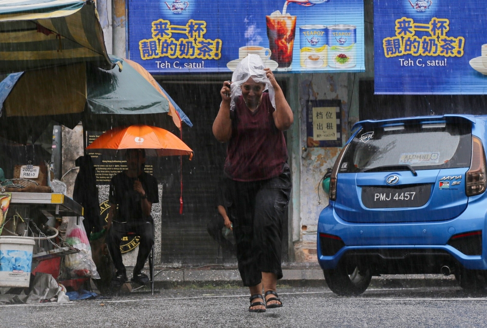 A woman shields her head with a plastic sheet while crossing a road during a downpour in Ipoh, Perak on August 3, 2024. — Bernama pic