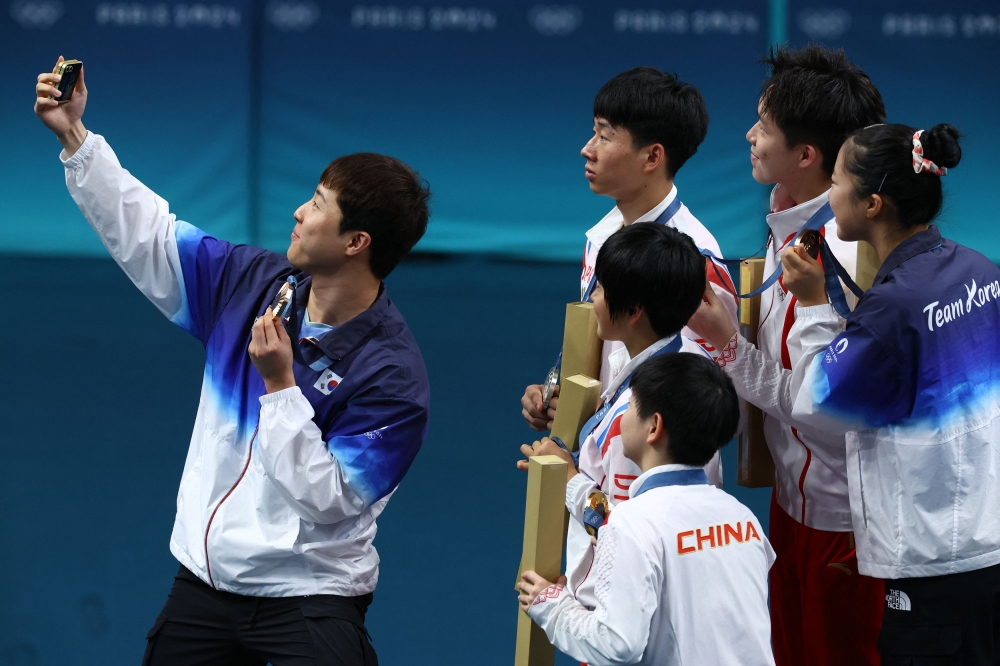 South Korea's Lim Jong-hoon takes a selfie with North Korea's Jong Sik Ri and Kum Yong Kim on the podium with their medals. Along with them is the Chinese team Wang Chuqin and Sun Yingsha. — Reuters pic