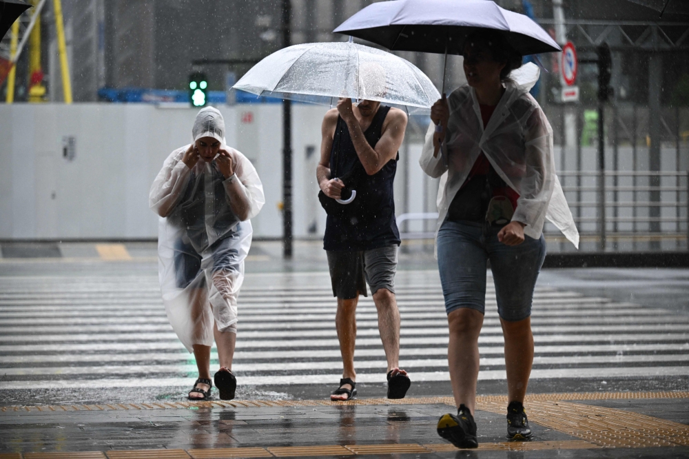 People wearing raincoats or holding umbrellas to shield from the heavy rain are seen outside Tokyo Station on August 16, 2024 as Typhoon Ampil barrels towards Japan's capital. — AFP pic