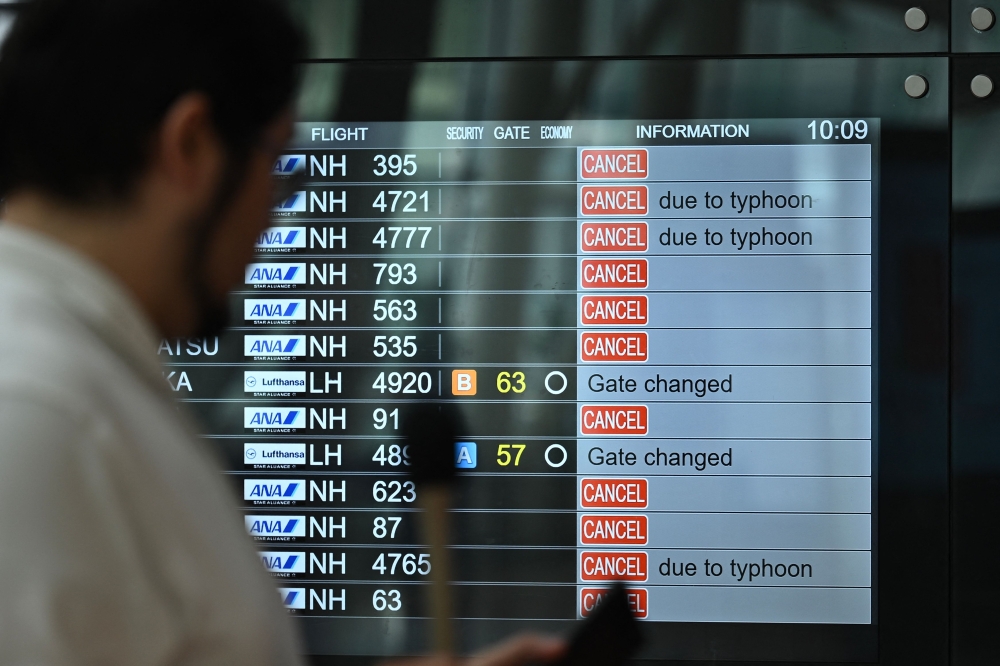 A TV news crew team works in front of a screen showing cancelled flights at the departure hall of Tokyo's Haneda Airport on August 16, 2024 as Typhoon Ampil barrels towards Japan's capital. — AFP pic